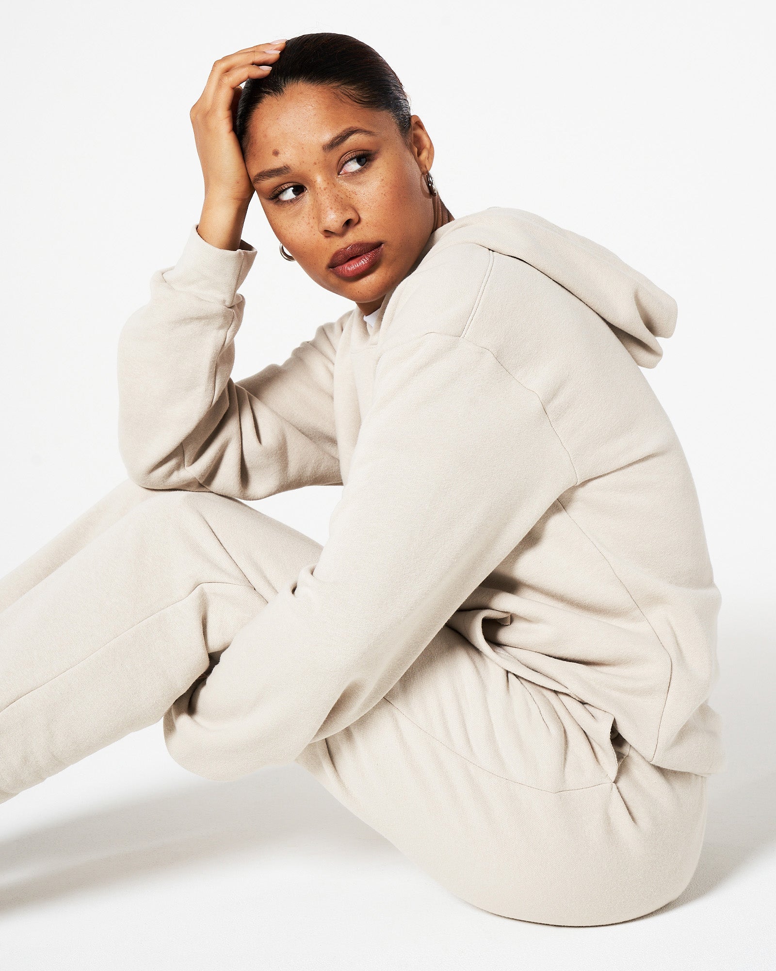 Female model sitting and wearing an American Apparel bone hoodie and sweatpants tracksuit set