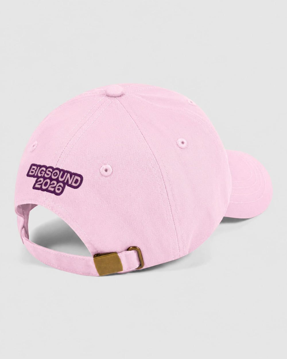 next image of BIGSOUND Dad Cap : A light pink baseball cap shown from a three quarters back angle on a light gray background. The cap features 'BIGSOUND 2026' embroidered in white text inside a dark purple oval patch on the side, with a matching pink adjustable strap and a small gold metal buckle -pink