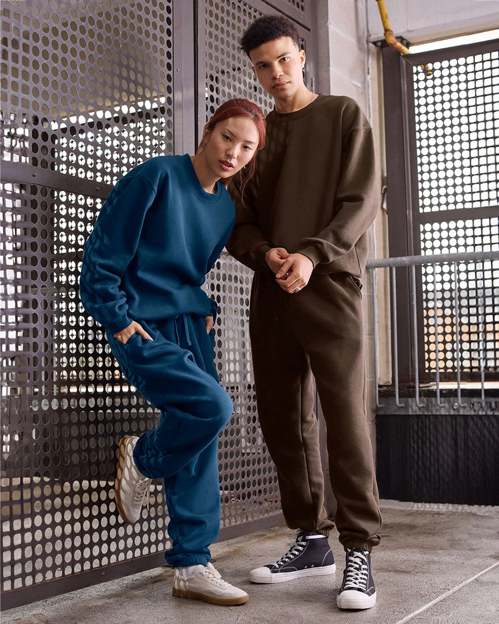 Two models in American Apparel unisex sweat sets pose stylishly in an urban industrial setting.