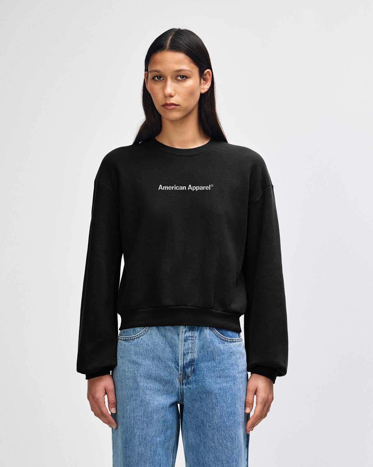 Person wearing a black sweatshirt and blue jeans on a light gray background -black