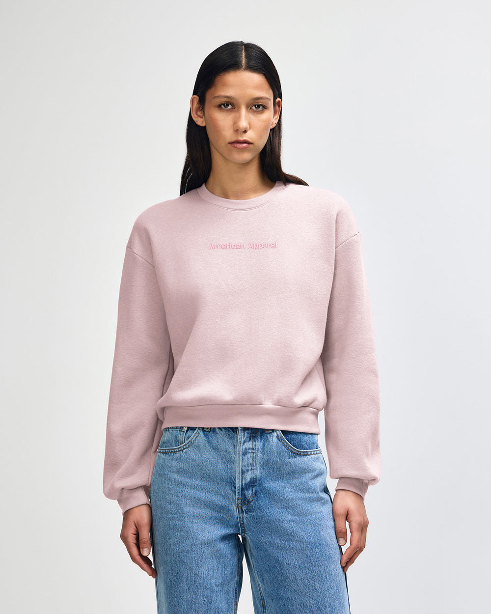 image of Women's Crop Sweatshirt Tracksuit Set - Embroidered Logo - Blush : Person wearing a light pink sweatshirt and blue jeans on a white background -blush