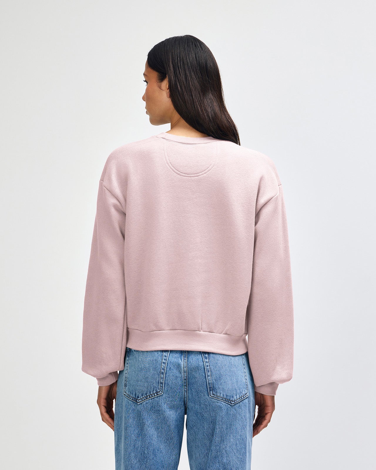 Person wearing a light pink sweatshirt and blue jeans on a white background -blush