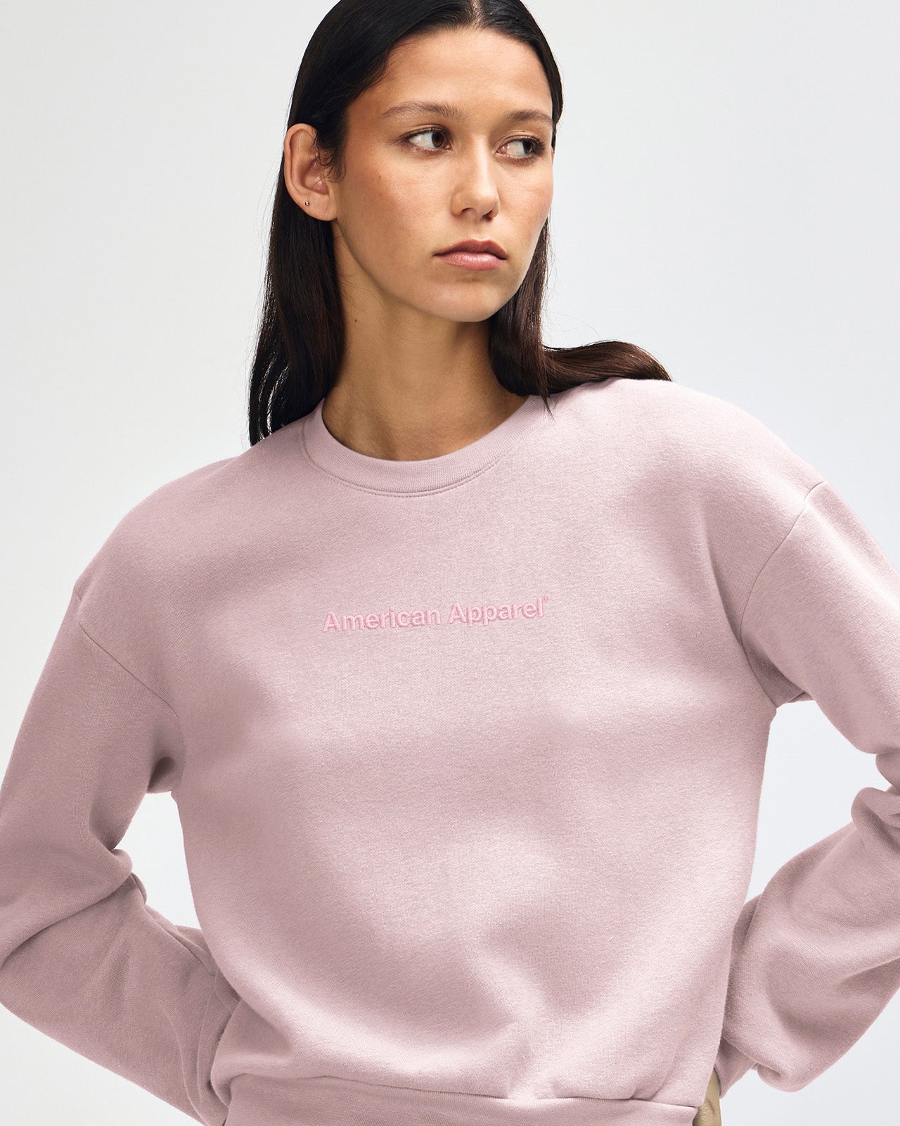 Woman wearing a pink sweatshirt with 'American Apparel' logo on a light gray background -blush