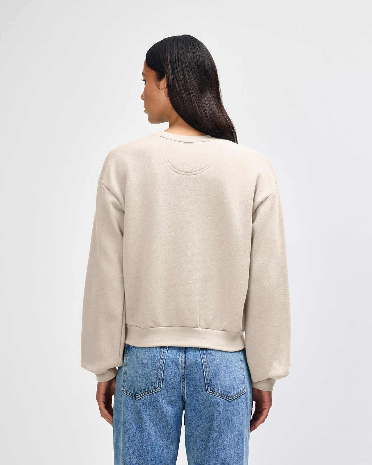 Model wearing a bone colour sweatshirt pairing with blue jeans (back pose) - bone