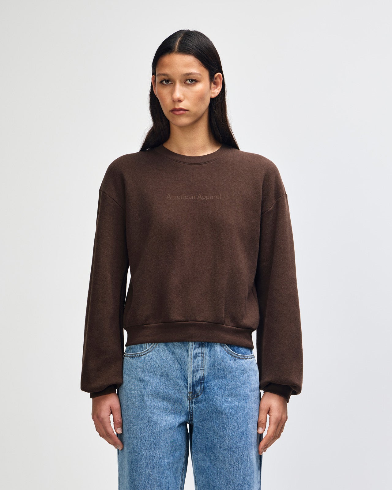 Person wearing a brown sweatshirt and blue jeans on a plain background -brown