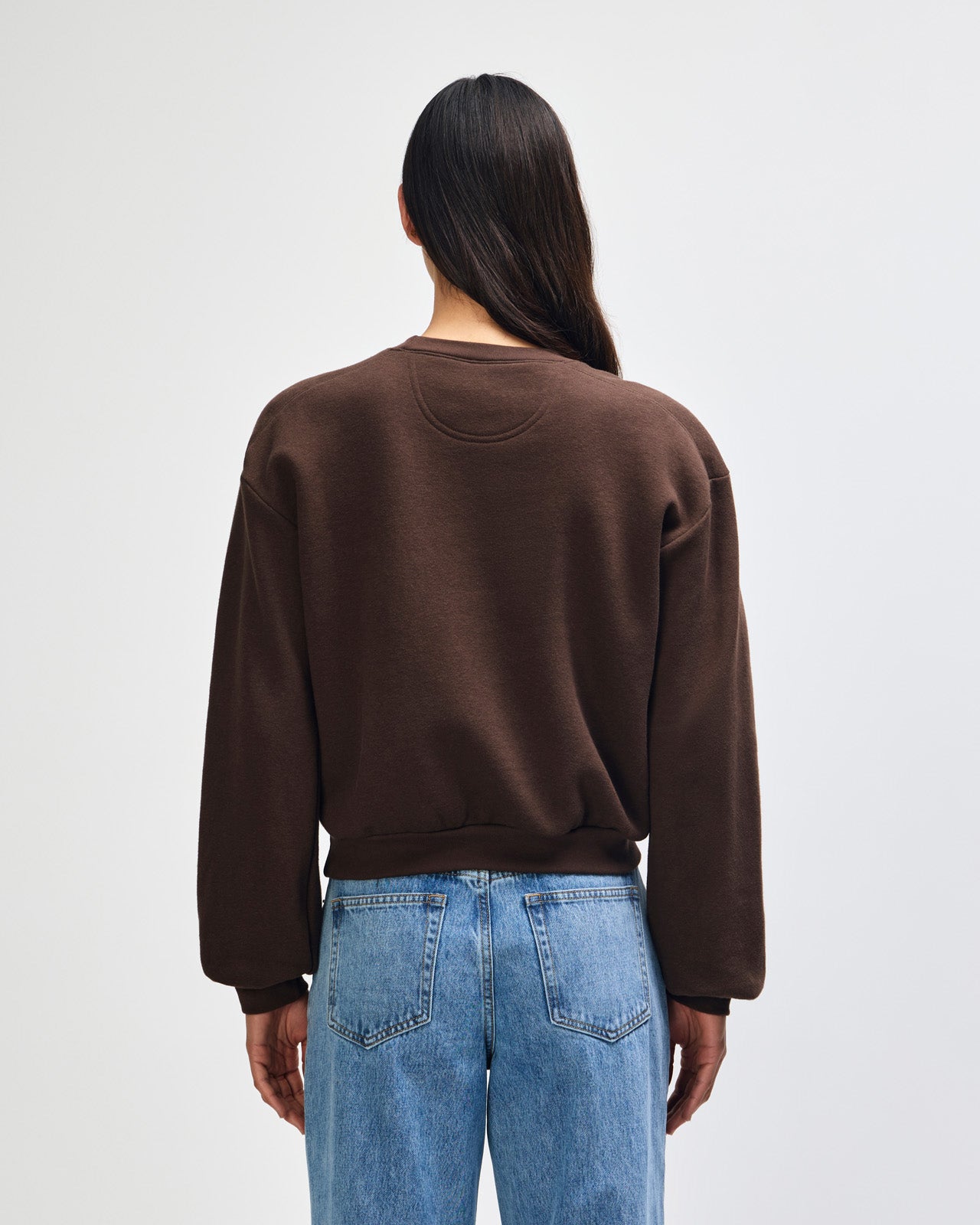 Person wearing a brown sweatshirt and blue jeans on a white background -brown