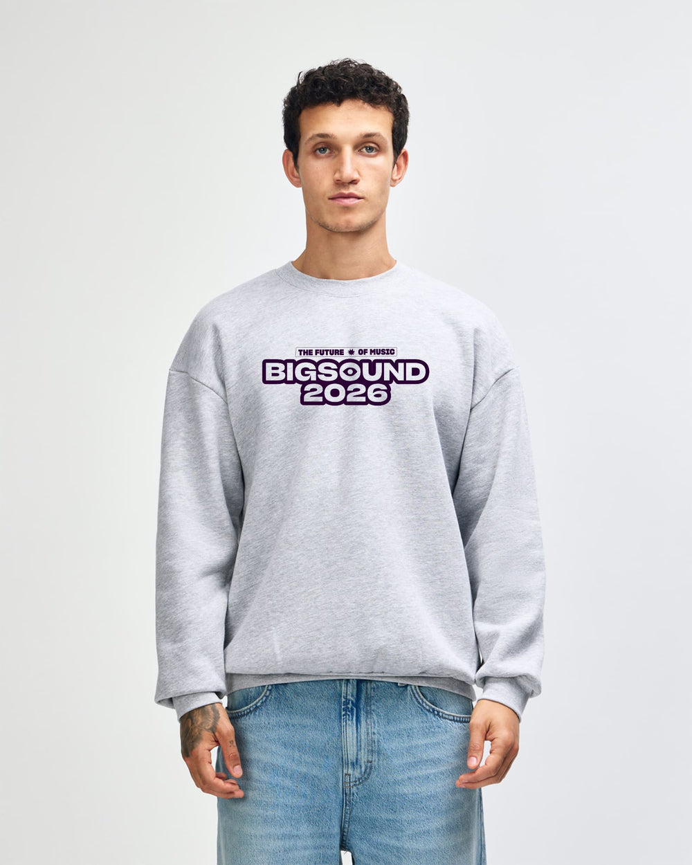 image of BIGSOUND Crewneck Sweatshirt : A man wearing a light gray crewneck sweatshirt with a 'BIGSOUND 2026' graphic on the chest, paired with blue jeans, standing against a light gray studio background -Heather Gray
