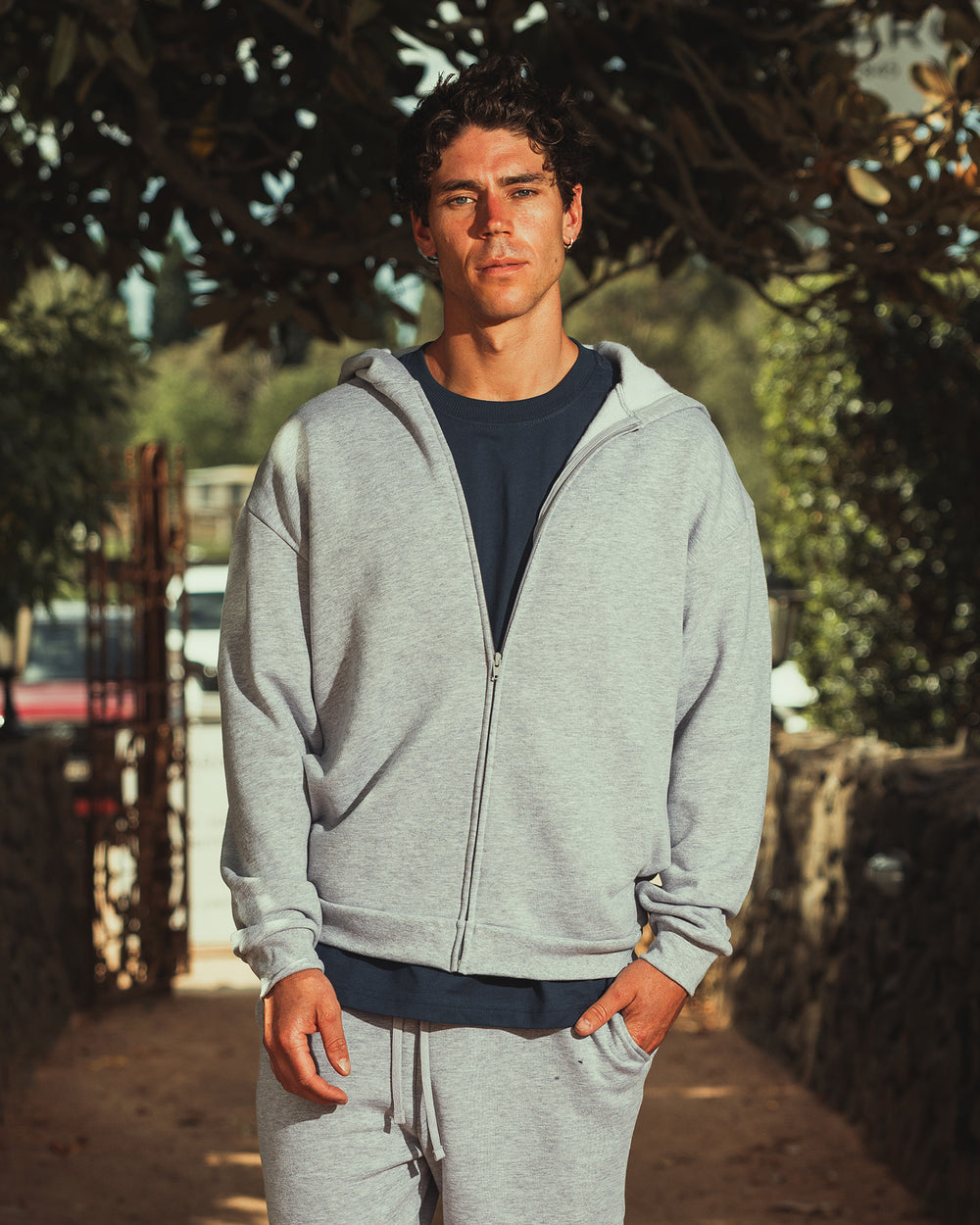 next image of Zip-Up Hoodie Tracksuit - Heather Grey : Male model wearing Reflex Unisex Full Zip Hooded Sweatshirt pairing with blue jeans (full length pose) -heather grey