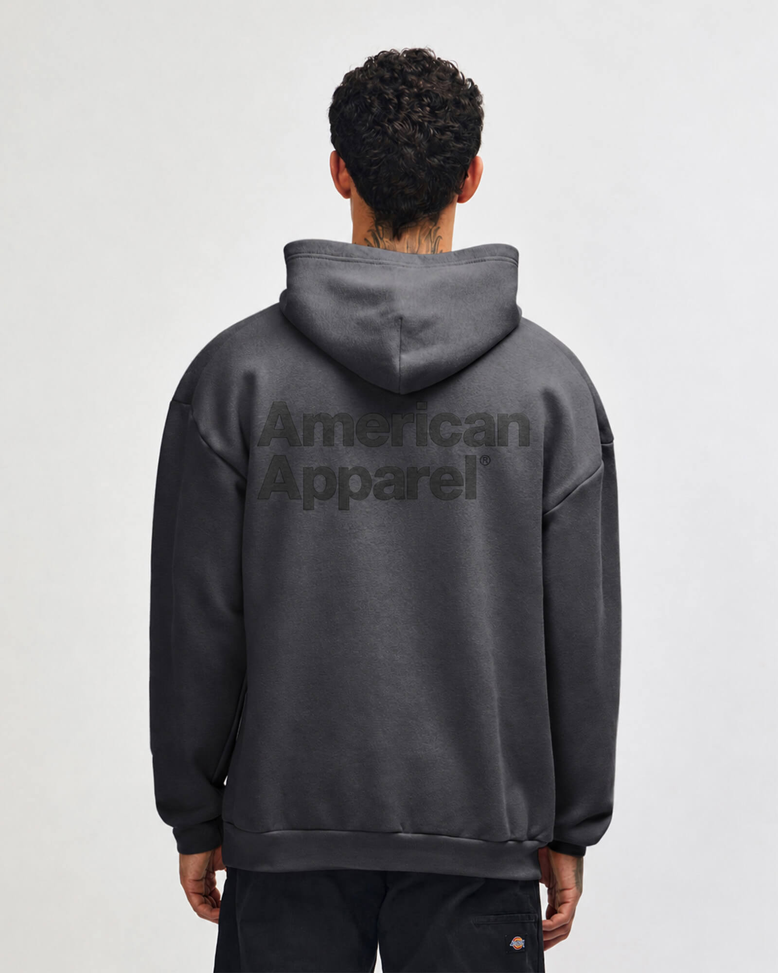 Person wearing a gray hoodie with 'American Apparel' logo on the back against a white background -Asphalt