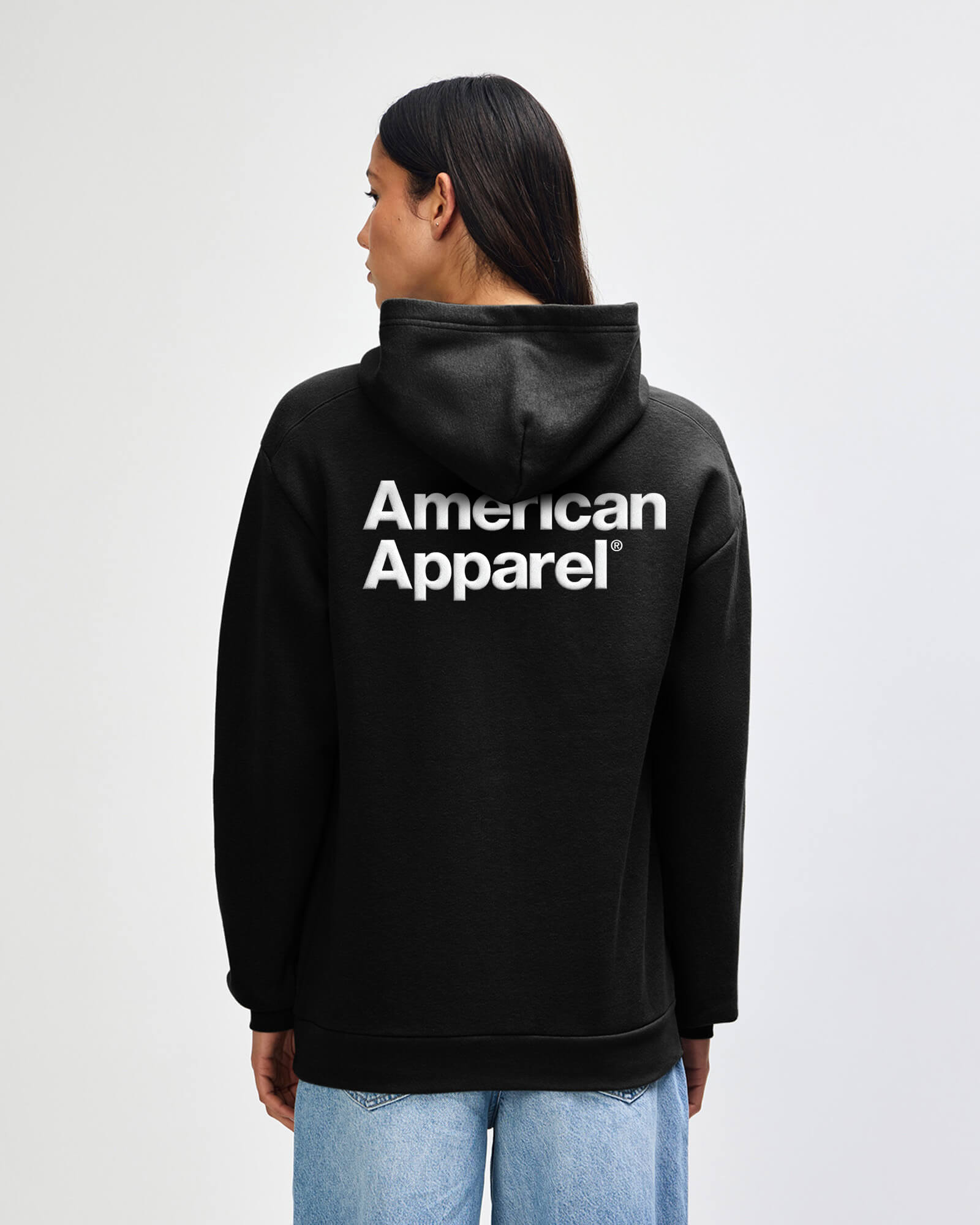 Person wearing a black hoodie with 'American Apparel' logo on the back against a white background -black