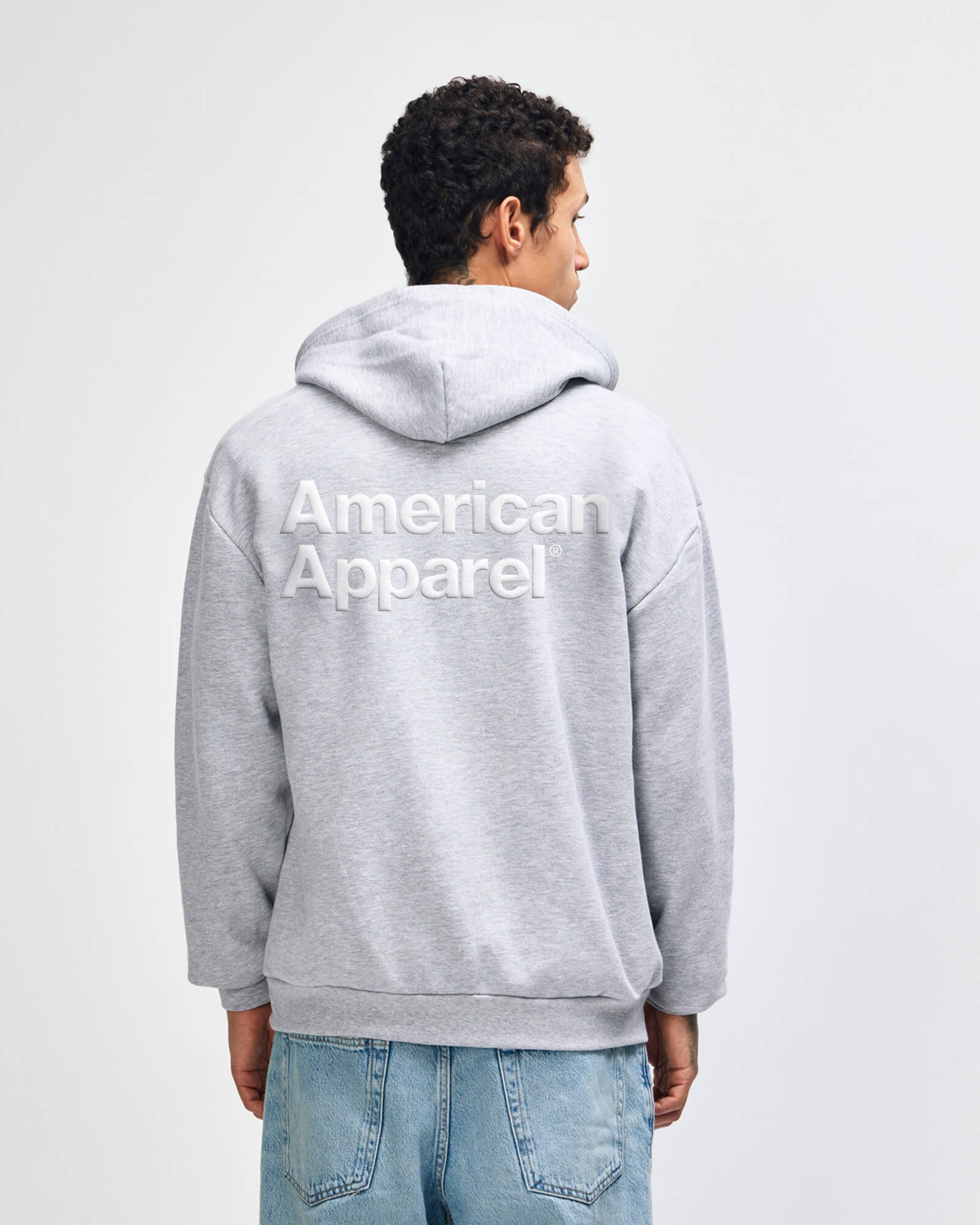 Person wearing a gray hoodie with 'American Apparel' logo on the back against a white background -Heather Grey